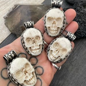 May include: Four white bone skull pendants with silver accents. Each pendant is carved with a detailed skull design and has a silver bail for hanging.