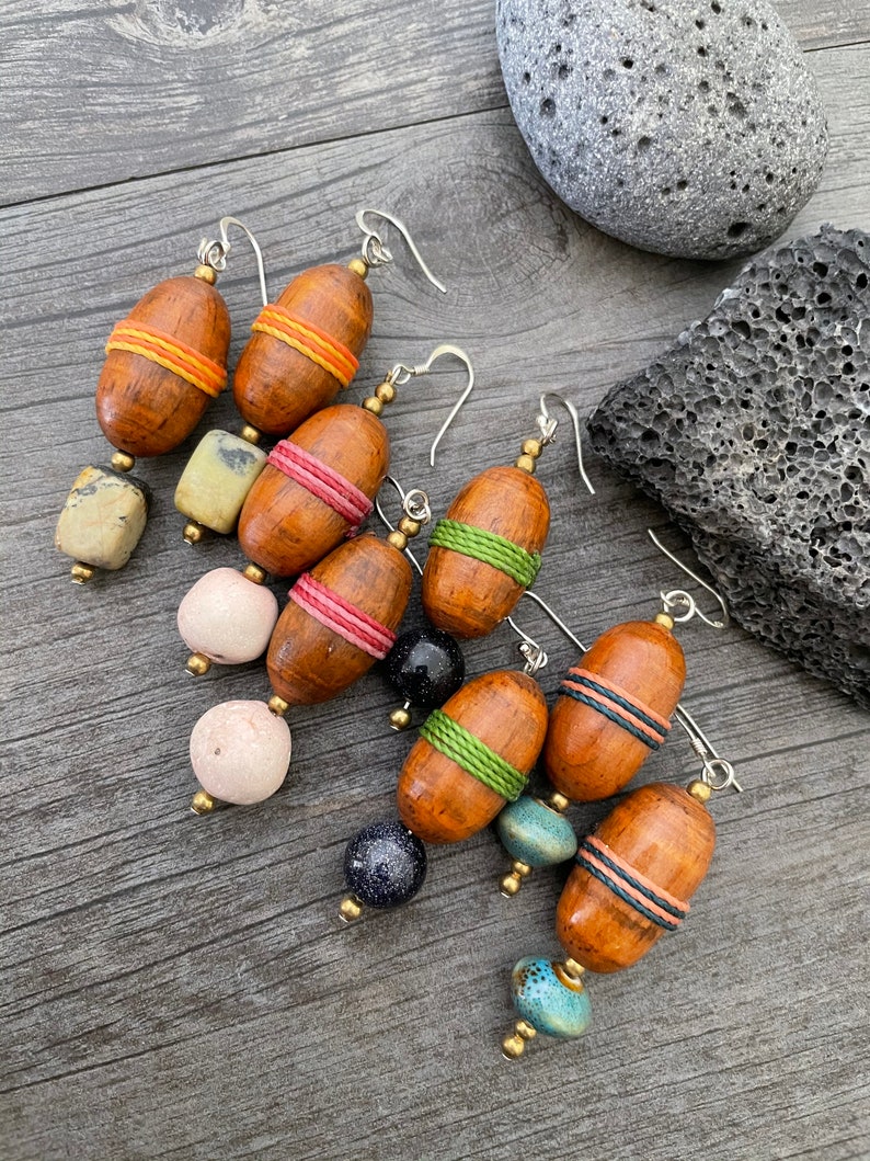 May include: A collection of handcrafted earrings featuring wooden acorn-shaped beads with colorful thread accents. The earrings have silver-colored ear wires and are paired with various stone and bead combinations. The wooden beads are approximately 1 inch in length.