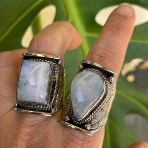 Puede incluir: Dos anillos de plata con engastes de piedra lunar. El anillo de la izquierda tiene una piedra lunar cuadrada, mientras que el anillo de la derecha tiene una piedra lunar en forma de lágrima.