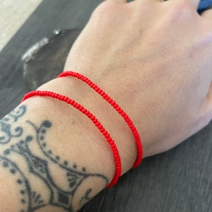 May include: Two red beaded bracelets on a person's wrist.