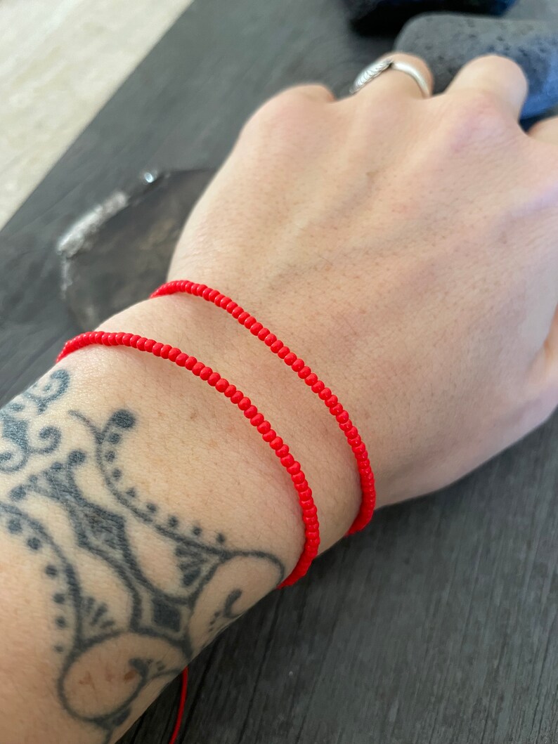 May include: Two red beaded bracelets on a person's wrist.