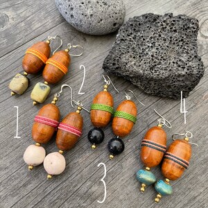 May include: Four pairs of handcrafted earrings with wooden barrel-shaped beads and colorful accents. Each pair features unique combinations of beads, including orange, pink, green, and blue, with silver-tone ear wires. The earrings are displayed on a wooden surface.
