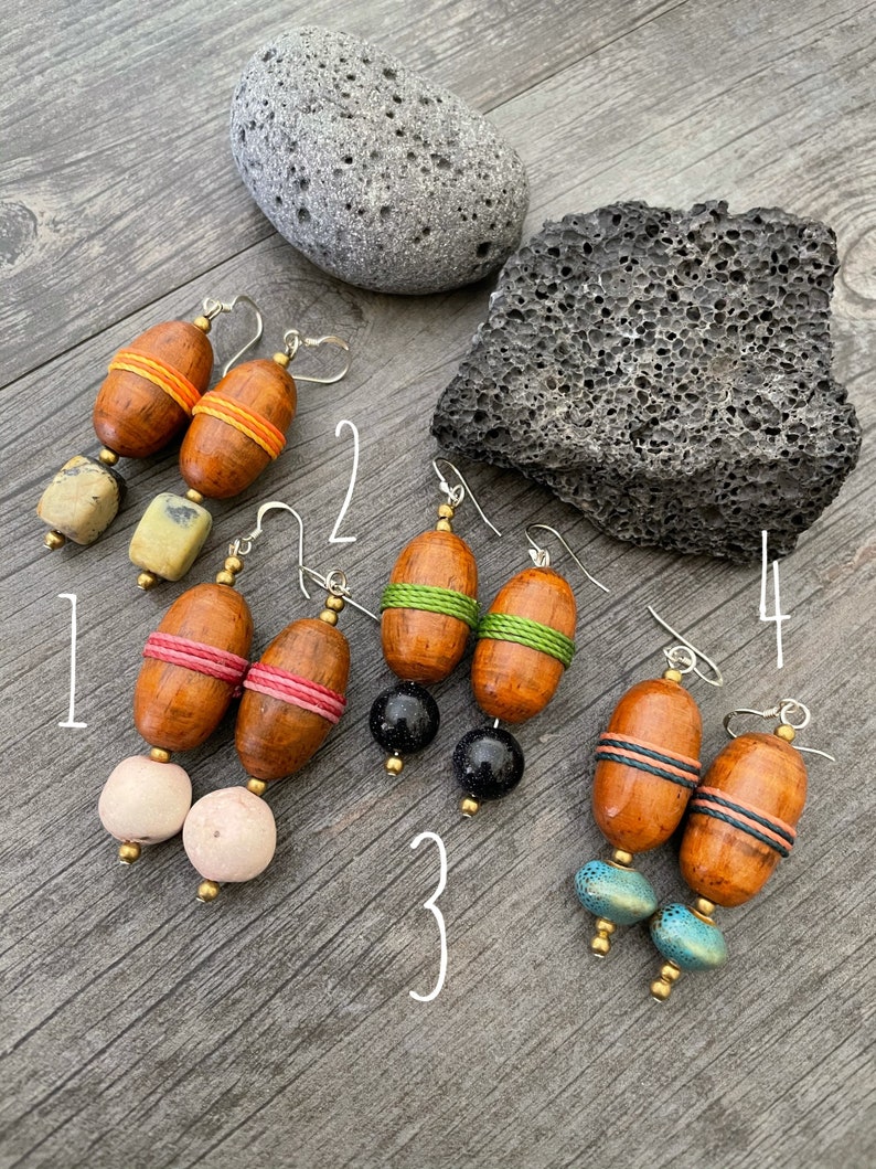 May include: Four pairs of handcrafted earrings with wooden barrel-shaped beads and colorful accents. Each pair features unique combinations of beads, including orange, pink, green, and blue, with silver-tone ear wires. The earrings are displayed on a wooden surface.