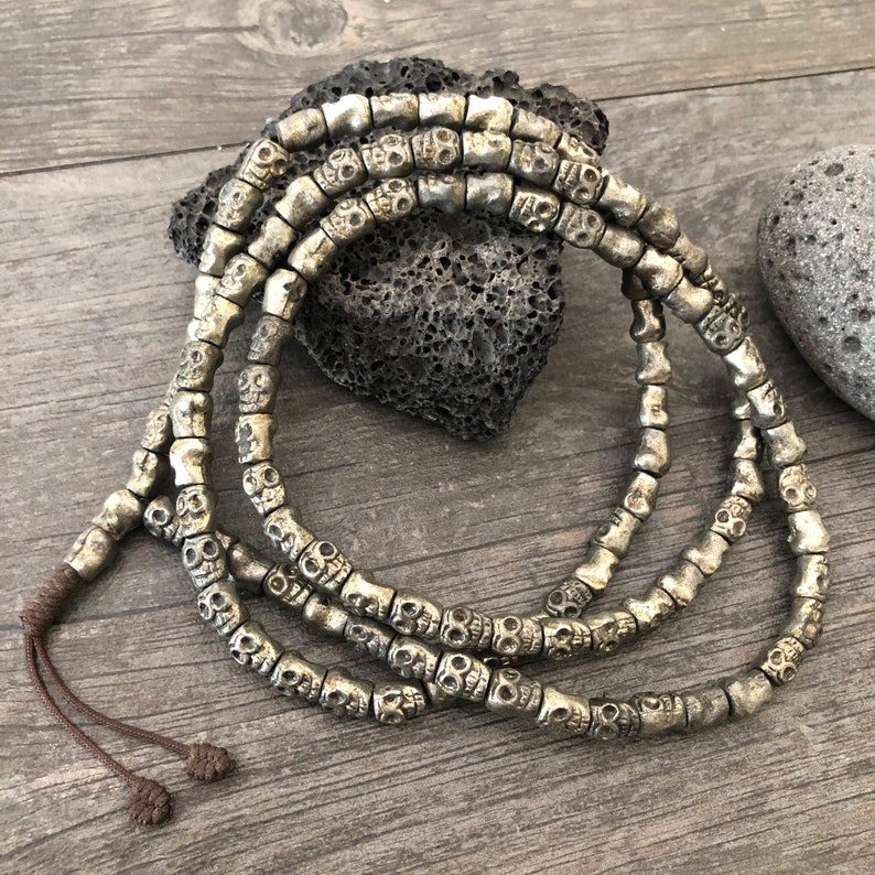 May include: A silver skull bead necklace with a dark brown cord. The necklace is made of many small skull beads that are all connected together.