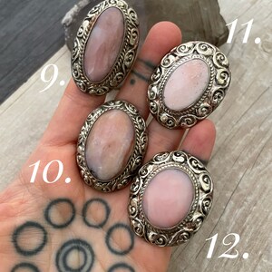 May include: Four oval-shaped pink opal rings with silver settings. The rings have intricate designs and are numbered 9, 10, 11, and 12.