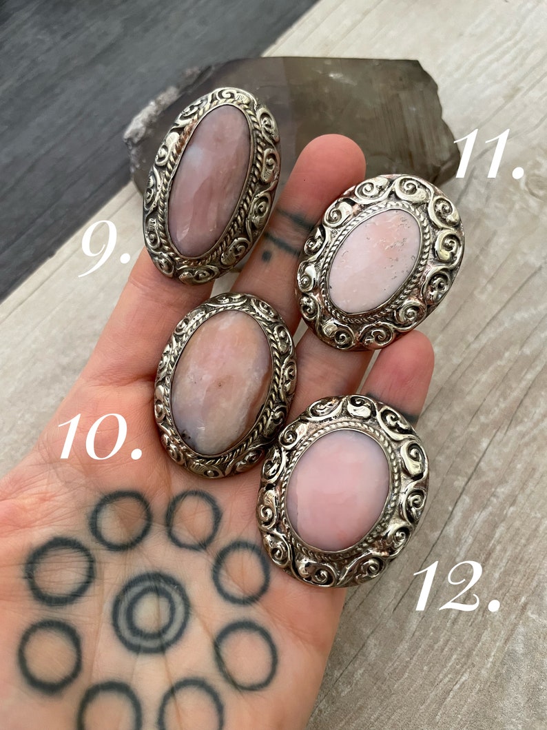 May include: Four oval-shaped pink opal rings with silver settings. The rings have intricate designs and are numbered 9, 10, 11, and 12.