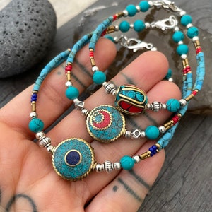 Puede incluir: Tres pulseras de cuentas turquesa y plata con diferentes piedras centrales de colores. Las piedras centrales son redondas y presentan dise&ntilde;os intrincados con piedras turquesa, rojas y azules.