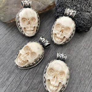 May include: Four white bone skull pendants with silver accents. Each pendant is carved with a detailed skull design and has a silver bail for hanging.