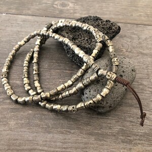 May include: A silver skull bead necklace with a brown leather cord. The necklace is made of small, round beads with a skull design.