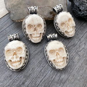 May include: Four white bone skull pendants with silver trim. Each pendant features a detailed skull design with eye sockets, a nose, and a mouth.
