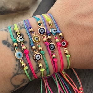 May include: A set of colorful string bracelets with gold beads and evil eye charms. The bracelets are in shades of pink, green, blue, and yellow.