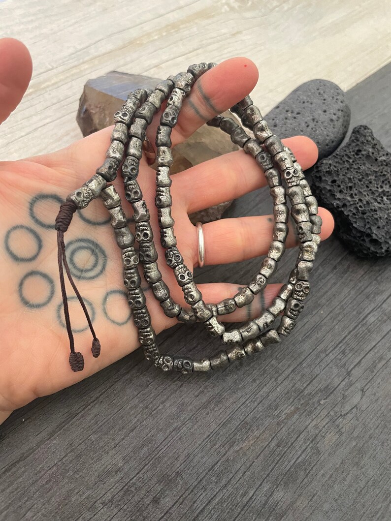 May include: A silver skull bead necklace with a brown leather cord. The necklace is made of many small skull beads and is about 18 inches long.