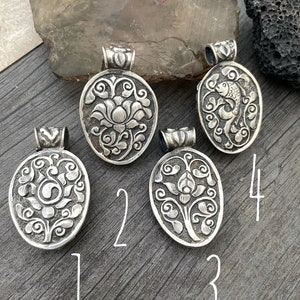 May include: Four silver pendants with intricate floral and fish designs. The pendants are numbered 1 through 4.