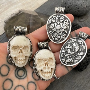 May include: Four silver pendants with intricate designs. Two pendants feature a skull design, while the other two feature floral and fish designs.