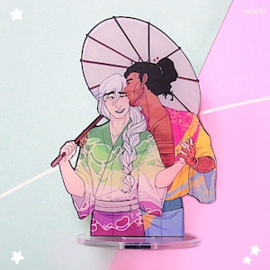 May include: A vibrant illustration of two figures in embrace, one with white hair and a green kimono, the other with dark hair and a pink kimono. They are holding hands under a white parasol. The artwork is mounted on a clear stand.