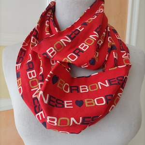 May include: A red infinity scarf with the word "BORBONESE" in white, gold, and navy blue letters. The scarf is wrapped around a mannequin and features a repeating pattern with heart symbols.