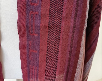 May include: A close-up of a burgundy scarf with a striped pattern. The scarf features vertical stripes in varying shades of red and purple, with a black zigzag pattern and fringed edges. The word "ECHO" is visible.