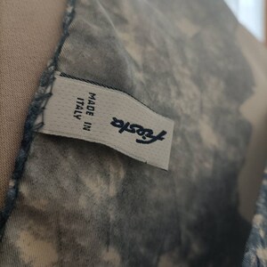 May include: Close-up of a fabric with a blue and white pattern. A label with the word "Fiesta" and "MADE IN ITALY" is visible. The fabric has a textured appearance.