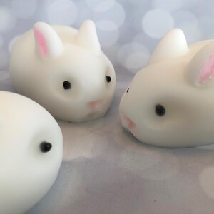 There are three white bunnies with black eyes, pink ears, and noses.  These bunny soaps appear to have a smooth texture.