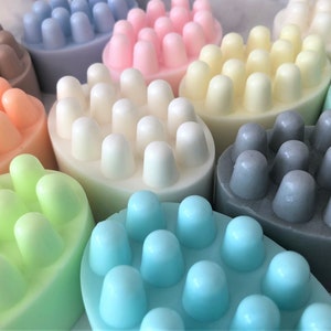 May include: Assortment of colorful massage soap bars with textured bumps. The bars are in shades of light blue, pink, beige, light green, peach, and gray.