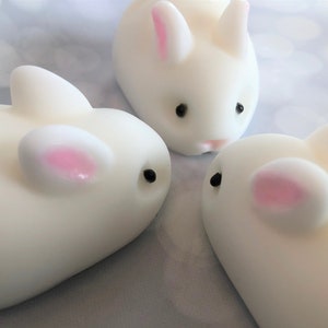 There are three white bunnies with black eyes, pink ears, and noses.  These bunny soaps appear to have a smooth texture.