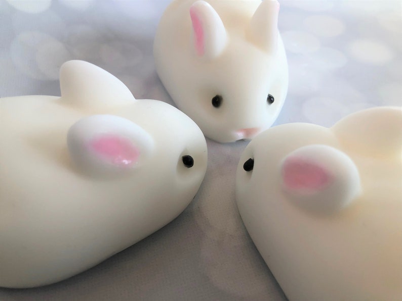 There are three white bunnies with black eyes, pink ears, and noses.  These bunny soaps appear to have a smooth texture.