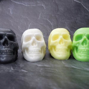 four skull soaps colors sitting in a row.  from left to right gray, white, yellow and green.