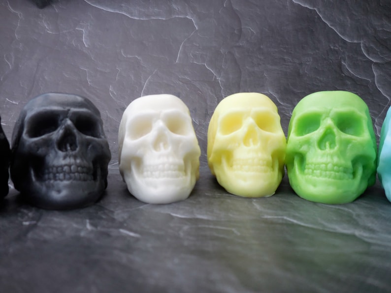 four skull soaps colors sitting in a row.  from left to right gray, white, yellow and green.