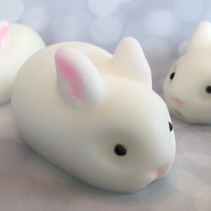 There are three white bunnies with black eyes, pink ears, and noses.  These bunny soaps appear to have a smooth texture.