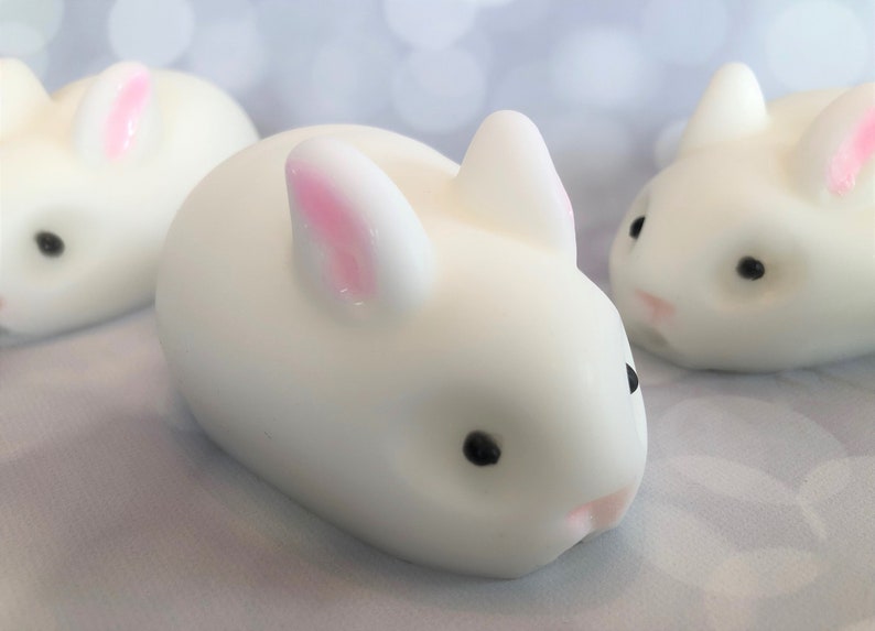 There are three white bunnies with black eyes, pink ears, and noses.  These bunny soaps appear to have a smooth texture.