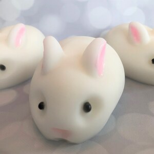 There are three white bunnies with black eyes, pink ears, and noses.  These bunny soaps appear to have a smooth texture.