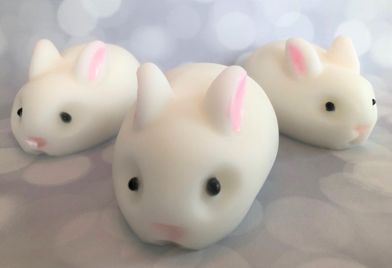 There are three white bunnies with black eyes, pink ears, and noses.  These bunny soaps appear to have a smooth texture.