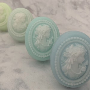 An oval mini soap featuring the illustration of a sophisticated woman facing in one direction, rendered in soft pastel colors of your choice with white highlights that enhance her elegance and charm.