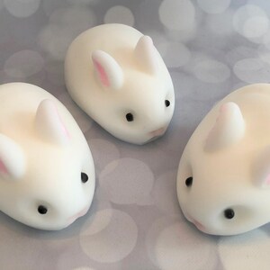 There are three white bunnies with black eyes, pink ears, and noses.  These bunny soaps appear to have a smooth texture.