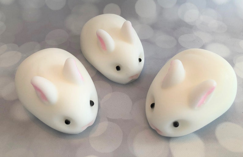 There are three white bunnies with black eyes, pink ears, and noses.  These bunny soaps appear to have a smooth texture.