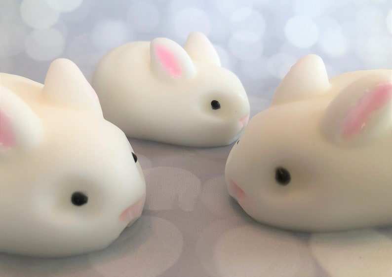 There are three white bunnies with black eyes, pink ears, and noses.  These bunny soaps appear to have a smooth texture.