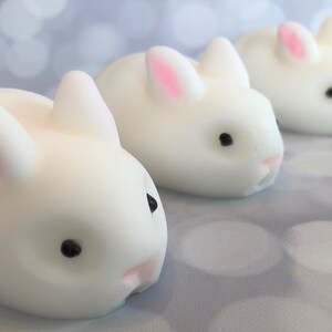 There are three white bunnies with black eyes, pink ears, and noses.  These bunny soaps appear to have a smooth texture.