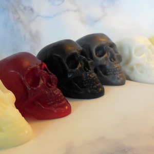 A close up view of six of the color options available for these skull soaps.  From left to right glow in the dark, transparent red (looks like skull shaped jello), black, gray, white, yellow.