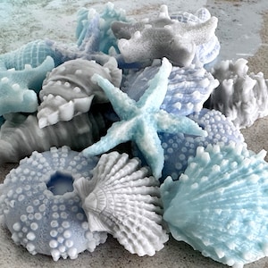 May include: A collection of blue and gray seashell-shaped candles. The candles are arranged in a pile and include starfish, clams, and sea urchins.