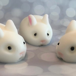 There are three white bunnies with black eyes, pink ears, and noses.  These bunny soaps appear to have a smooth texture.