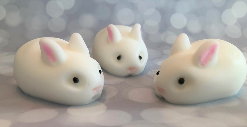 There are three white bunnies with black eyes, pink ears, and noses.  These bunny soaps appear to have a smooth texture.