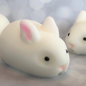 There are three white bunnies with black eyes, pink ears, and noses.  These bunny soaps appear to have a smooth texture.