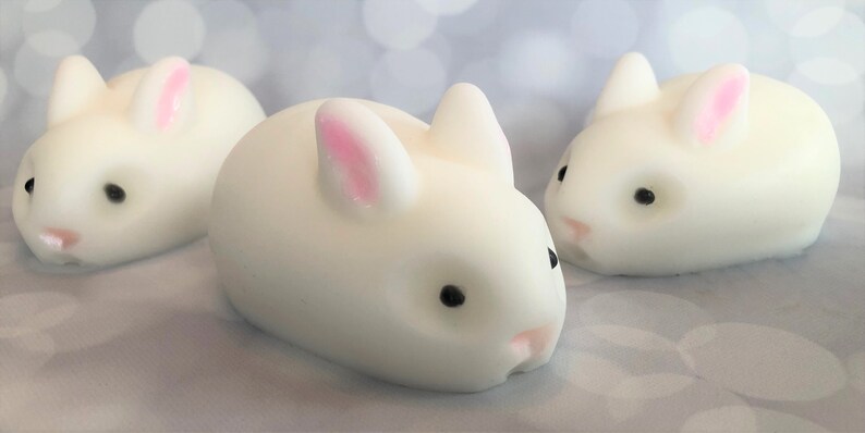 There are three white bunnies with black eyes, pink ears, and noses.  These bunny soaps appear to have a smooth texture.