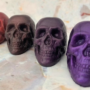 Diagonal row of 4 skulls from back left to front right (colors red wine, black-red which is a blend of black and red producing a very deep shade of red, purple eggplant which is a deep color similar to eggplant skin, and lastly purple galaxy.