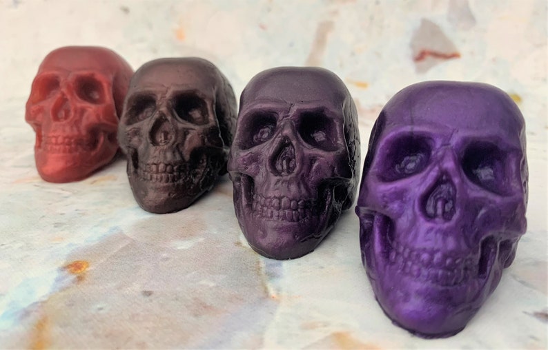 Diagonal row of 4 skulls from back left to front right (colors red wine, black-red which is a blend of black and red producing a very deep shade of red, purple eggplant which is a deep color similar to eggplant skin, and lastly purple galaxy.