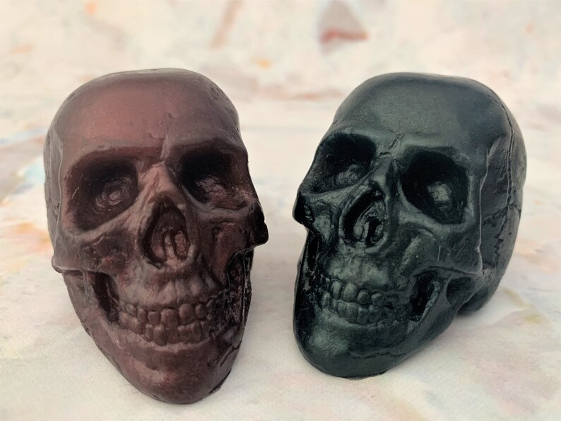 Two skulls sitting next to each other facing a bit inward.  The skull on the left is black-red which is a deep blend of black and red.  The skull on the right is black-green which is a deep blend of black and green.
