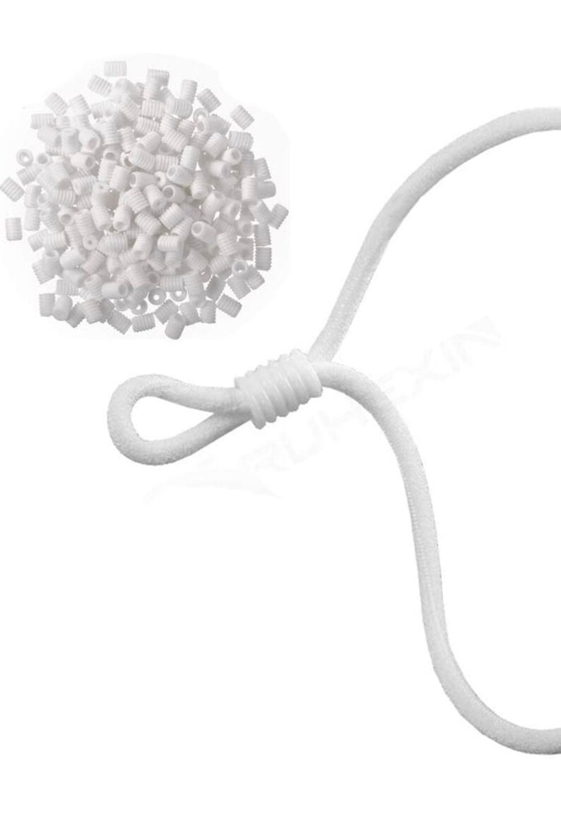 May include: A collection of small, white plastic cord adjusters and a white elastic cord. The adjusters are cylindrical with a hole through the center. The elastic cord is looped and knotted, designed for face masks or similar items.