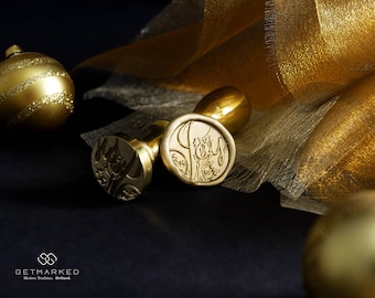 May include: Two gold wax seals with a decorative design. The seals are on a black surface with a gold fabric in the background.