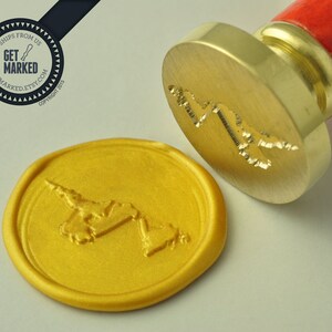 Op de afbeelding: Een goudkleurige waszegelstempel met een ontwerp van een gestileerde wereldkaart. De stempel wordt gebruikt om een ​​waszegel op een stuk papier te maken. De waszegel is goudkleurig.