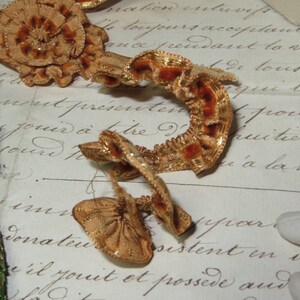 May include: A close-up of a gold and brown velvet ribbon with a ruffled edge. The ribbon is lying on a piece of paper with handwritten text.